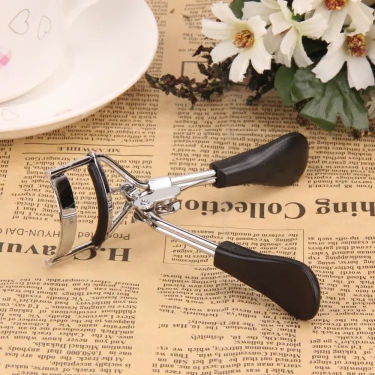 Eyelash curler on a newspaper background with flowers and a bowl.