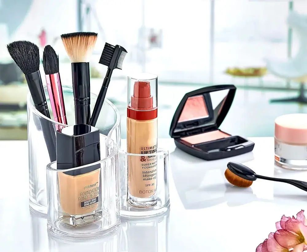 Clear acrylic makeup organizer tray filled with brushes and cosmetics on a vanity